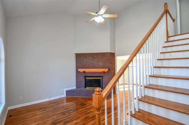 stairway featuring a brick fireplace, ceiling fan, high vaulted ceiling, and hardwood / wood-style flooring