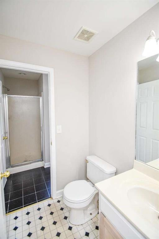 bathroom featuring tile patterned floors, vanity, toilet, and a shower with shower door