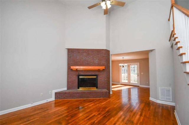 unfurnished living room with hardwood / wood-style flooring, ceiling fan, a fireplace, and a high ceiling