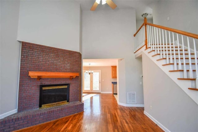 unfurnished living room with hardwood / wood-style floors, ceiling fan with notable chandelier, a towering ceiling, and a fireplace