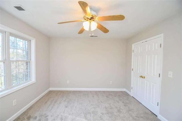 unfurnished room featuring ceiling fan, light carpet, and a wealth of natural light