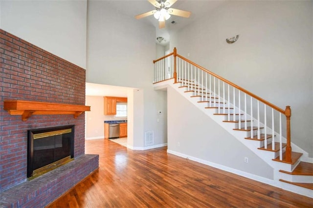 unfurnished living room featuring ceiling fan, a fireplace, wood-type flooring, and a high ceiling