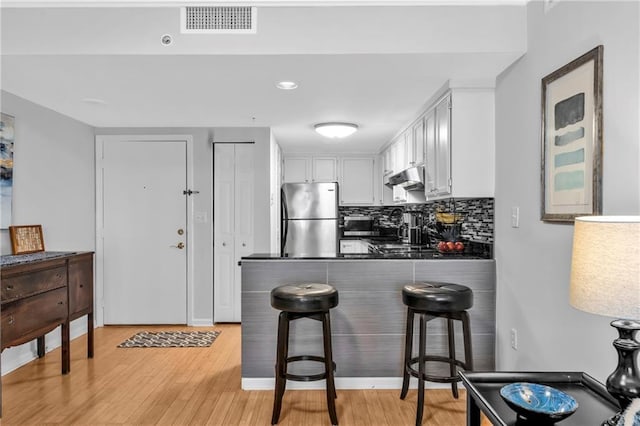 199 14th St NE Unit 2010, Atlanta, GA 30309 - kitchen with under cabinet range hood, a peninsula, backsplash, freestanding refrigerator, and dark countertops