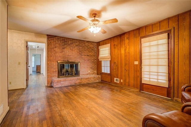 1850 Francis Rd SW, Conyers, GA 30094 - unfurnished living room with a fireplace, wood walls, a ceiling fan, wood finished floors, and visible vents