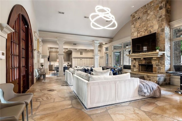 living room featuring ornate columns, a notable chandelier, vaulted ceiling, and a fireplace