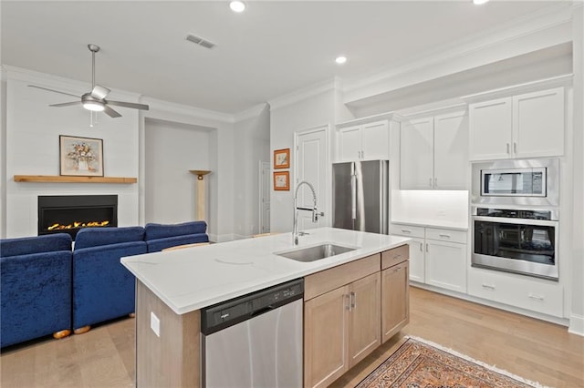 kitchen with an island with sink, stainless steel appliances, sink, light wood-type flooring, and white cabinetry