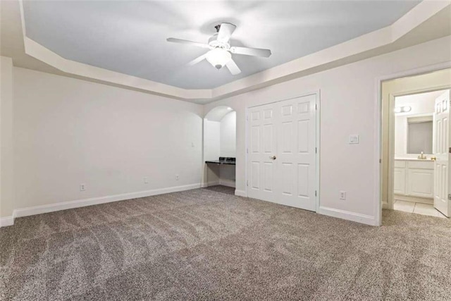 unfurnished bedroom with a tray ceiling, ceiling fan, a closet, and light colored carpet