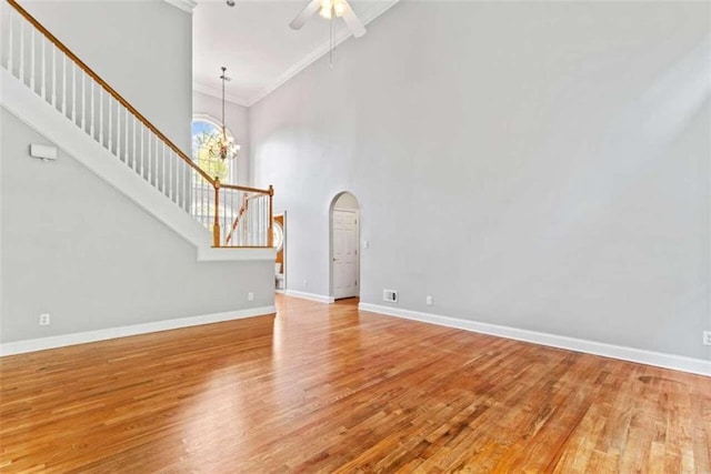 unfurnished living room featuring ceiling fan with notable chandelier, a towering ceiling, light hardwood / wood-style flooring, and crown molding