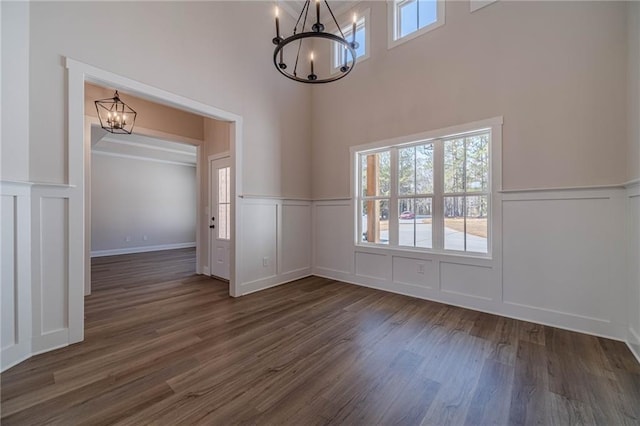 unfurnished dining area featuring a wainscoted wall, a decorative wall, a notable chandelier, and dark wood-style flooring