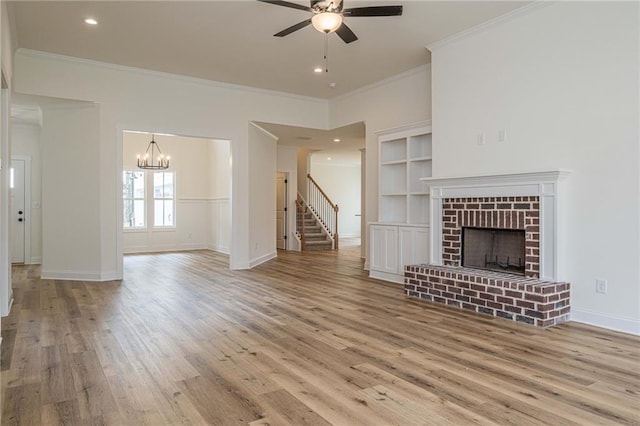 unfurnished living room featuring light wood finished floors, built in shelves, ornamental molding, a fireplace, and a ceiling fan