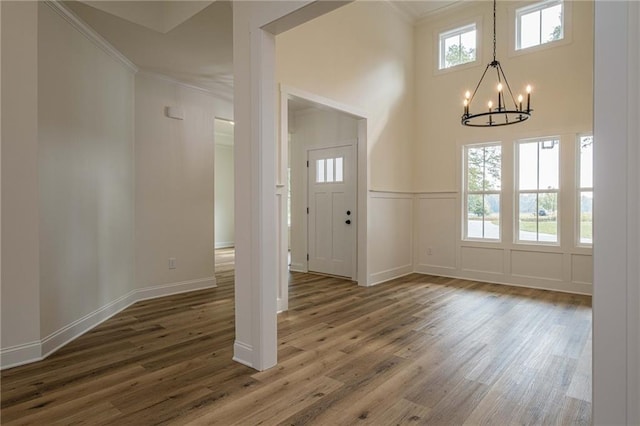 entrance foyer with a chandelier, a decorative wall, ornamental molding, and wood finished floors