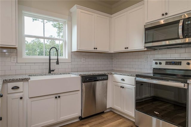 kitchen with tasteful backsplash, light wood finished floors, appliances with stainless steel finishes, white cabinets, and a sink