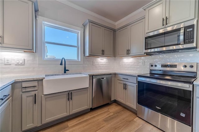 kitchen with gray cabinetry, ornamental molding, decorative backsplash, appliances with stainless steel finishes, and a sink