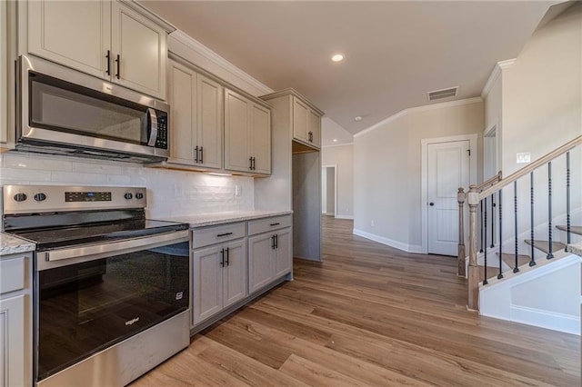 kitchen featuring crown molding, light wood-type flooring, decorative backsplash, gray cabinets, and appliances with stainless steel finishes