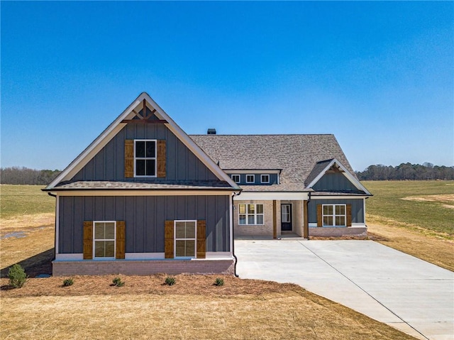 view of front facade with board and batten siding, concrete driveway, a front lawn, and a shingled roof