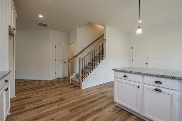 kitchen with light stone countertops, visible vents, light wood finished floors, ornamental molding, and white cabinets