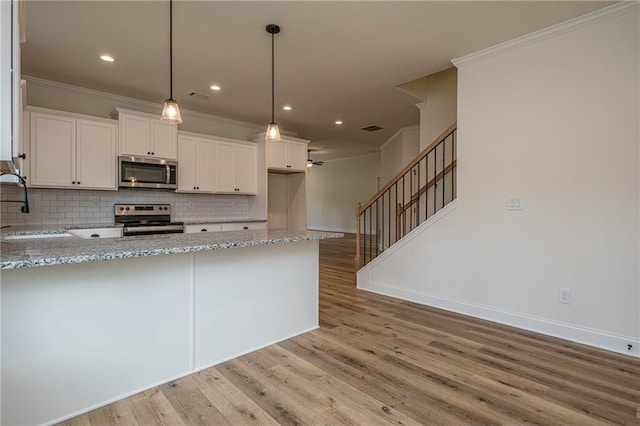 kitchen with light wood finished floors, stainless steel appliances, crown molding, and light stone countertops