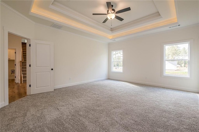 carpeted empty room with a ceiling fan, baseboards, visible vents, a tray ceiling, and crown molding