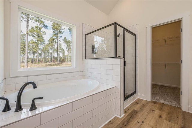 bathroom with a walk in closet, wood finished floors, a garden tub, and a stall shower