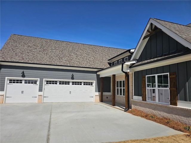 view of side of property with board and batten siding, concrete driveway, an attached garage, a shingled roof, and brick siding