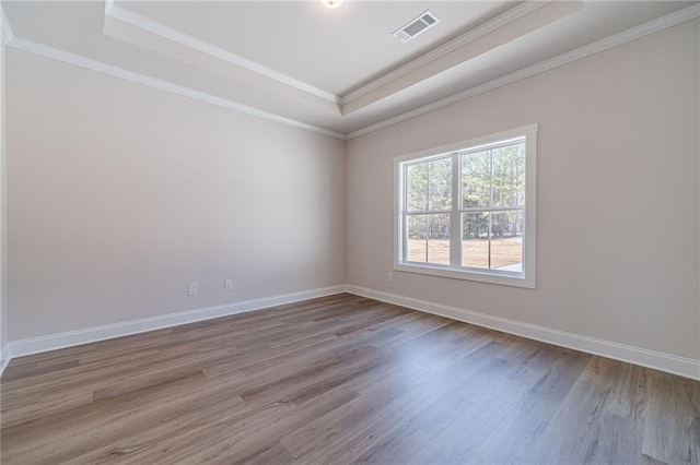 spare room featuring wood finished floors, visible vents, baseboards, crown molding, and a raised ceiling