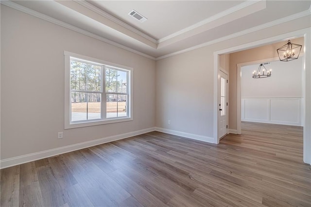 empty room featuring visible vents, a tray ceiling, wood finished floors, crown molding, and a chandelier