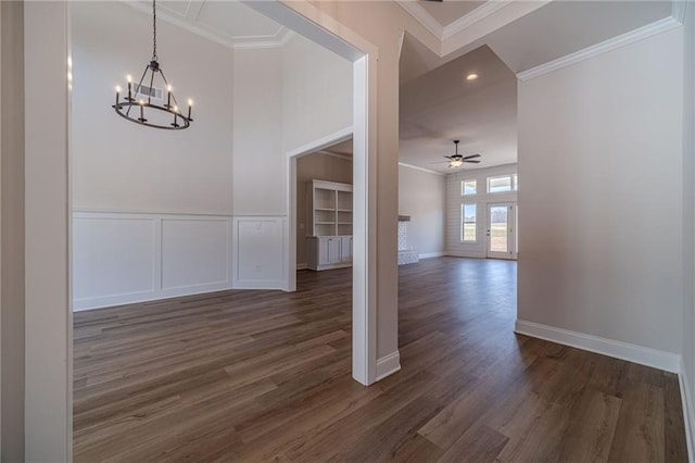 unfurnished dining area with ceiling fan with notable chandelier, dark wood finished floors, wainscoting, a decorative wall, and crown molding