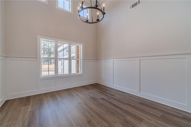 unfurnished room with dark wood finished floors, a healthy amount of sunlight, visible vents, and a chandelier