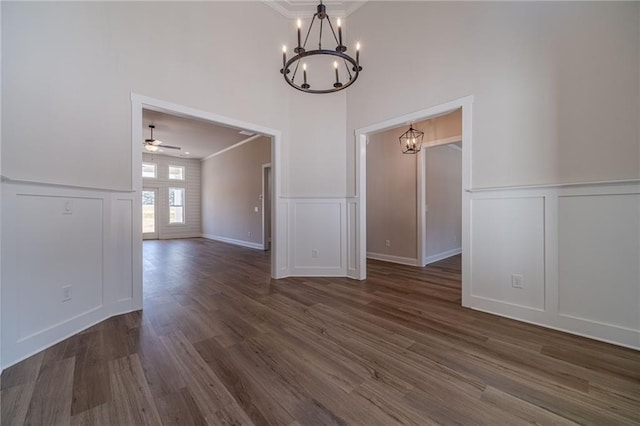 unfurnished room featuring a decorative wall, ornamental molding, dark wood-style flooring, and ceiling fan with notable chandelier