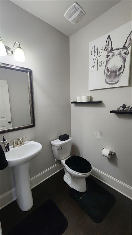 half bath featuring baseboards, visible vents, and toilet