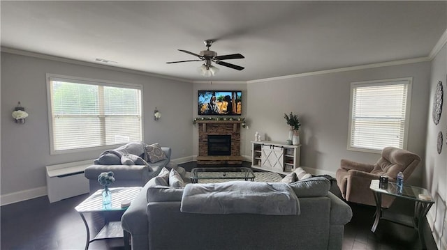 living area with wood finished floors, ceiling fan, a stone fireplace, baseboards, and crown molding