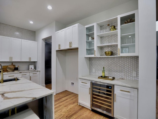 kitchen with light stone countertops, white cabinets, beverage cooler, and light wood-type flooring