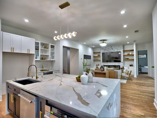 kitchen featuring light stone countertops, sink, pendant lighting, a fireplace, and white cabinets