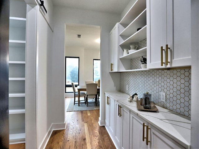 bar with light stone countertops, decorative backsplash, wood-type flooring, a barn door, and white cabinetry