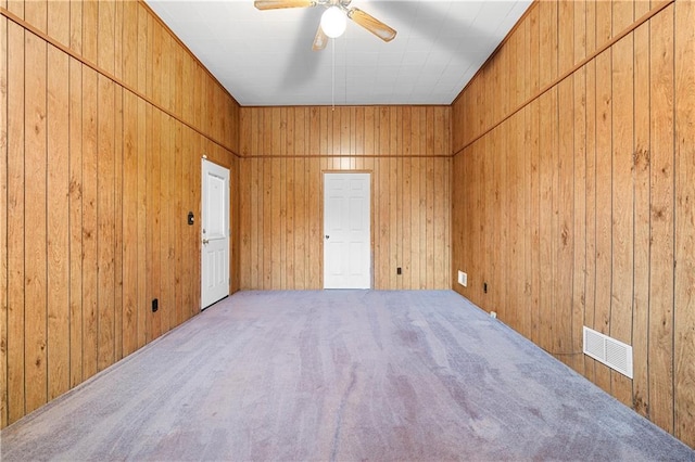 spare room featuring ceiling fan, carpet, visible vents, and wooden walls