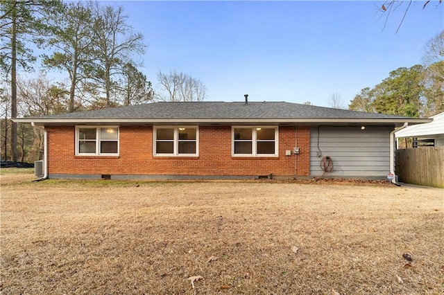 rear view of house featuring roof with shingles, brick siding, a yard, and fence