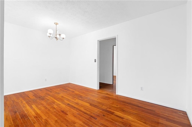 unfurnished room featuring baseboards, a notable chandelier, and hardwood / wood-style floors