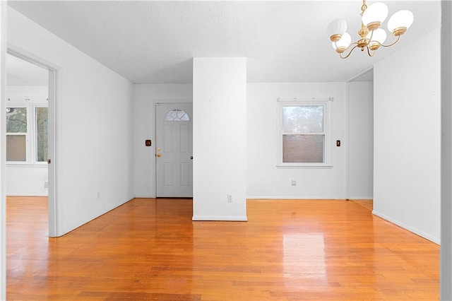 unfurnished room with light wood-style flooring, a textured ceiling, a chandelier, and baseboards