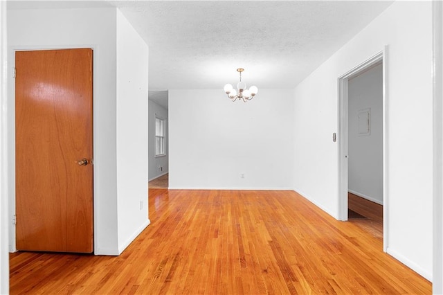 spare room with light wood-type flooring, a textured ceiling, baseboards, and a notable chandelier