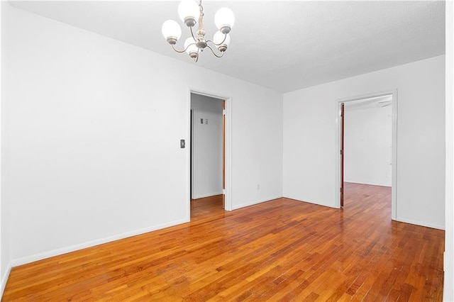 empty room featuring a chandelier, hardwood / wood-style floors, and baseboards