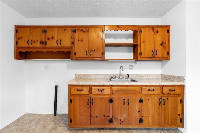 kitchen featuring brown cabinets, light countertops, a textured ceiling, open shelves, and a sink