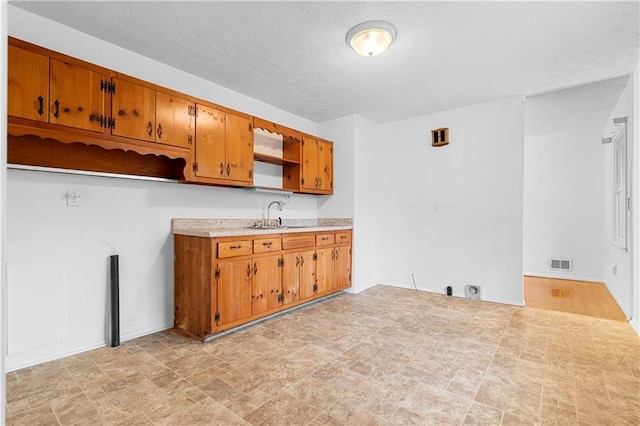 kitchen with visible vents, brown cabinets, a sink, and light countertops