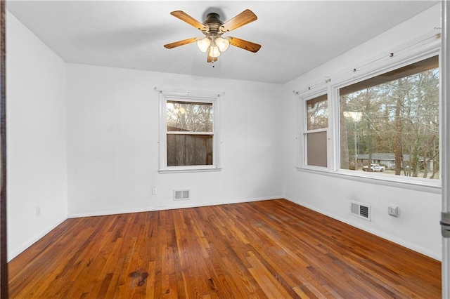 unfurnished room featuring a healthy amount of sunlight, visible vents, and hardwood / wood-style floors