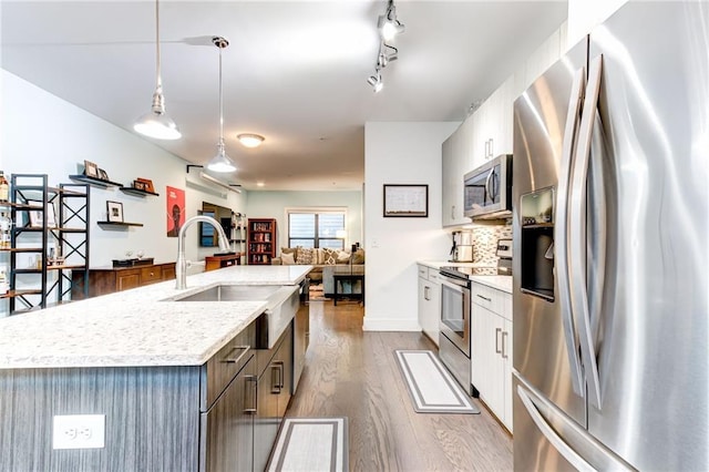 kitchen with a center island with sink, light hardwood / wood-style flooring, pendant lighting, stainless steel appliances, and white cabinets