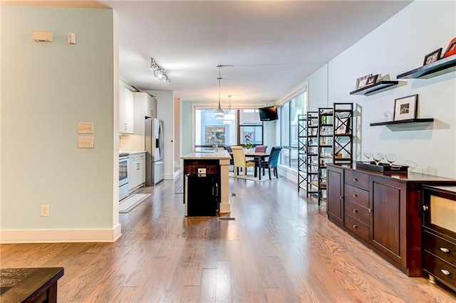 kitchen featuring a breakfast bar, stainless steel refrigerator with ice dispenser, a center island, light wood-type flooring, and decorative light fixtures