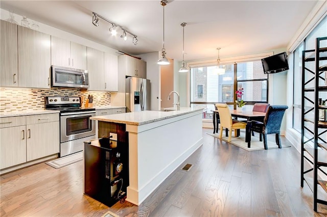 kitchen featuring a center island with sink, light hardwood / wood-style flooring, decorative light fixtures, backsplash, and appliances with stainless steel finishes