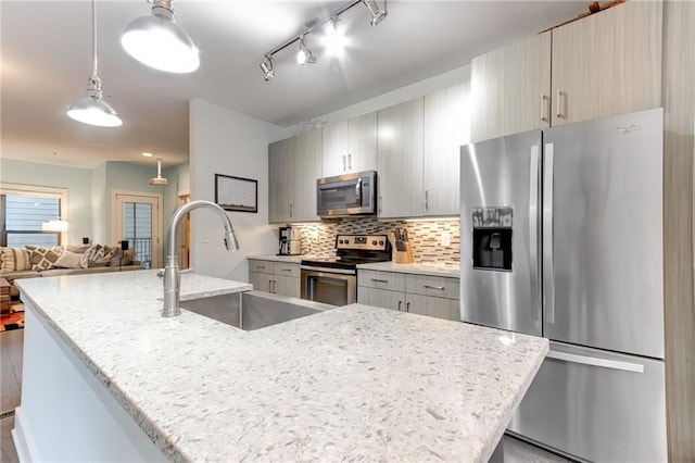 kitchen with appliances with stainless steel finishes, tasteful backsplash, light stone counters, pendant lighting, and sink