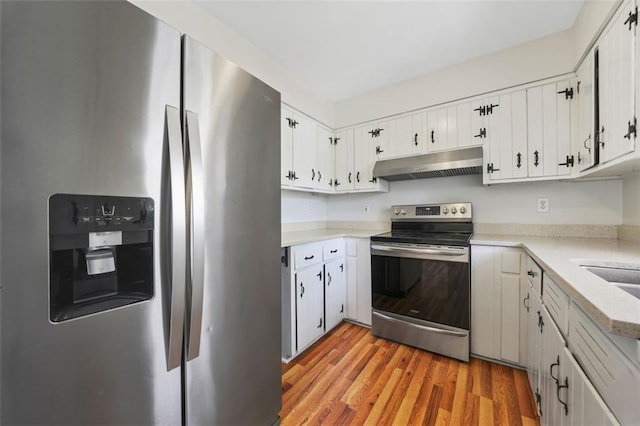 kitchen with light wood finished floors, light countertops, under cabinet range hood, appliances with stainless steel finishes, and white cabinetry