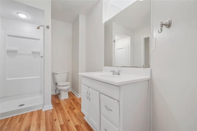 bathroom featuring toilet, wood finished floors, a shower, baseboards, and vanity