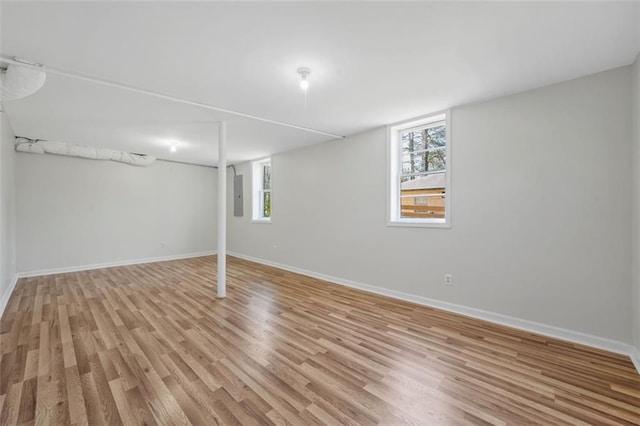 below grade area featuring electric panel, light wood-type flooring, and a healthy amount of sunlight